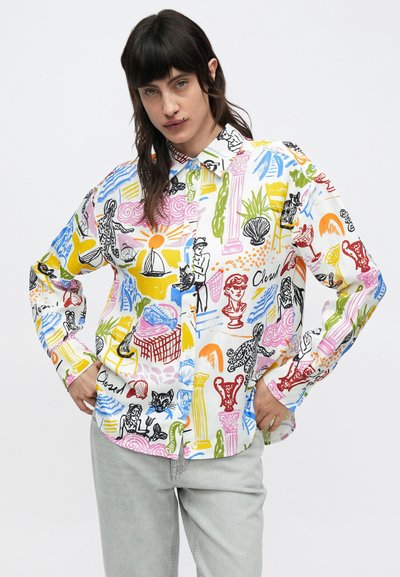 Chemise à manches longues, boutonnée, en tissu blanc avec des imprimés graphiques colorés représentant des personnages, des plantes et des objets en nuances de noir, jaune et rose.