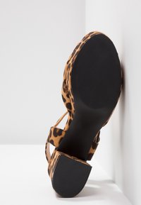 Sandale pour femme à talon bloc avec imprimé léopard, vue de la semelle contre un fond blanc d'angle.