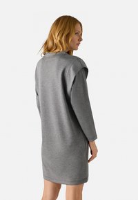 Vestido sudadera gris de corte relajado, con mangas largas y hombros caídos. Textura suave, a la altura de la rodilla y diseño minimalista.