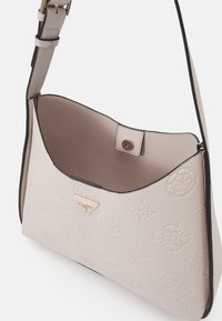 Borsa a spalla beige chiaro realizzata in pelle texturizzata, con un accento del logo dorato, forma arrotondata e un bordo scuro a contrasto.