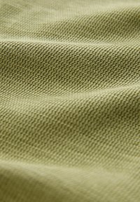 Közelkép hullámos, bordázott mintázatú, texturált zöld szövetből, amelyen lágy redők és finom árnyékok láthatók.