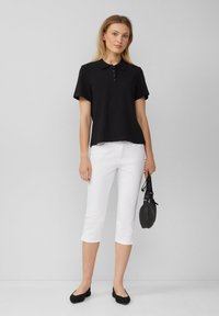 Polo noir à manches courtes avec patte de boutonnage, associé à un pantalon blanc cropped et des ballerines noires. Accessoire : petit sac à main noir.