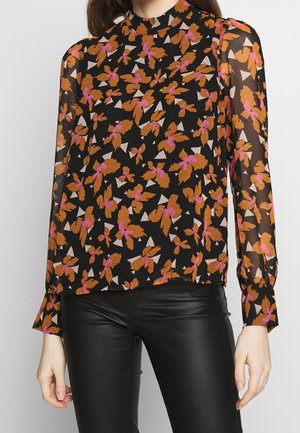 Schwarze, durchsichtige Bluse mit mehrfarbigen Blumen- und geometrischen Mustern, hohem Kragen, langen Ärmeln und eng anliegenden Manschetten. Kombiniert mit schwarzen Hosen.
