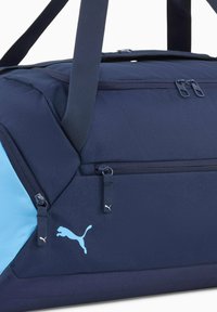 Bolsa de viaje navy hecha de tejido duradero con acentos en azul claro, que cuenta con cierres de doble cremallera, un bolsillo frontal y el logo de Puma.