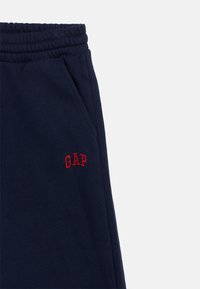 Tengerészkék melegítőnadrág rugalmas derékpánttal, két oldalzsebbel és piros hímzett "GAP" logóval a bal combon. Puha pamut anyag.