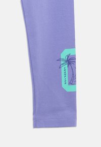 Λιλά ύφασμα με ένα τιρκουάζ γράμμα "C" που έχει έναν φοίνικα και τη λέξη "Champion" τυπωμένα κοντά στο τελείωμα.