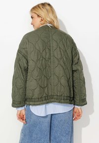 Veste matelassée vert olive en forme ronde, dotée d'une surface texturée et d'un ourlet côtelé. Portez-la par-dessus une chemise rayée bleu clair et un jean en denim.