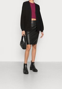 Černý pletený cardigan, vínový crop top, černá kožená tužková sukně. Černá pletená kabelka a kotníkové boty s masivním podpatkem.