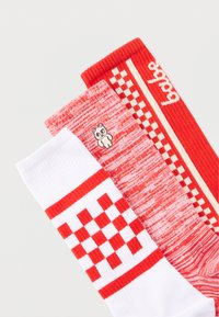 Τρία διπλωμένα ζευγάρια κάλτσες σε κόκκινο και λευκό: μία με καρό σχέδιο, μία μαρλεμένη με μικρή εικονογράφηση αρκούδας, και μία ριγέ με γραπτή λεπτομέρεια.