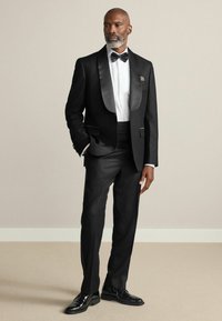 Black tuxedo with satin lapels, white dress shirt, and bow tie. Finished with black dress shoes, showcasing a tailored fit and sleek design.