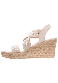 Sandale compensée beige avec plateforme en tissu tissé texturé. Dotée de brides croisées ornées de perles décoratives et de sequins.