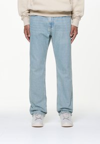 Hellblaue gerade geschnittene Jeans aus Denim-Material, mit dezenten Falten, leichter Ausbleichung und einem klassischen Fünf-Taschen-Design. Kombiniert mit hellen Sneakers.