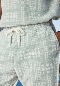Completo maglia e pantaloni di maglia verde chiaro con motivi geometrici bianchi. Vita con cordino, texture morbida e vestibilità rilassata.