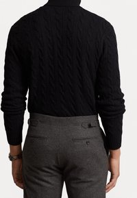 Czarny sweter z golfem wykonany z dzianiny warkoczowej z długimi rękawami, zestawiony z szarymi wełnianymi spodniami z tylnymi kieszeniami i regulowanymi paskami.