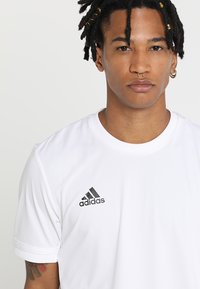 T-shirt sportivo bianco realizzato in materiale liscio e leggero. Presenta maniche corte e un logo Adidas nero sul lato sinistro del petto.