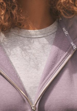 Violetinis zip-up džemperis su šviesiai pilku marškinėliu po juo. Džemperis turi sidabrinę užtrauktuką ir ženklą ant apvado. Matomi minkšti audinio tekstūrų elementai.