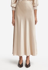 Satinbeige maxikjol med en slät textur och split på sidan. Kombinerad med mörka spetsiga skor som framhäver outfitens elegans.