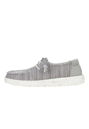 Chaussure slip-on tissée grise avec un panneau de talon gris clair, semelle parsemée de blanc et une caractéristique de laçage près du haut. Design plat, texture légère.