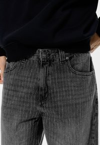 Jeans in denim grigio con motivo a righe verticali, design a cinque tasche e chiusura con bottone centrale in vita. Tessuto con finitura testurizzata.