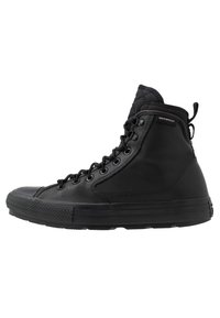 Svart vanntett høy-top sneakers laget av glatt materiale, med rund tå, snøring foran og teksturert gummisåle med mønsterdetaljer.