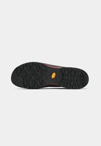 Suela de goma negra con un patrón de relieve en forma de diamante y pequeño logotipo de Vibram naranja en el centro de la suela del zapato.