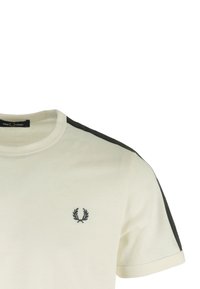 Camiseta de algodón crema con acentos negros en los hombros y un pequeño logo bordado en el lado izquierdo del pecho. Cuello redondo y mangas cortas.