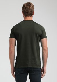 Donkergroene t-shirt met korte mouwen en een ronde hals, met een gladde textuur en een subtiele achternaaddetail. Gecombineerd met donkere jeans, gezien vanaf de achterkant.