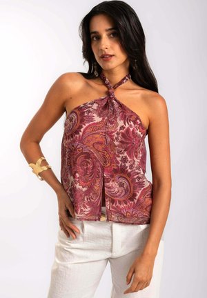Haut halter léger à motifs cachemire dans des teintes de bourgogne et de crème,avec un col noué et une silhouette fluide. Associé à un pantalon blanc.