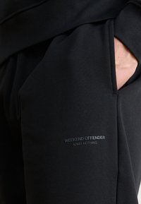 Pantaloni jogger neri realizzati in tessuto morbido, con una tasca laterale e un dettaglio in rilievo con il logo che recita "WEEKEND OFFENDER ADMIT NOTHING."