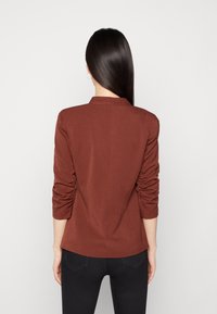 Hnědý, přiléhavý blejzr s dlouhými rukávy, řasením na loktech a límcem. Hladká tkanina, strukturovaný design, pohled ze vzadu.