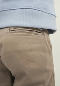 Ljusblå sweatshirt med ribbad nederkant ovanför khakifärgade byxor som har en strömlinjeformad bakficka, slät textur och ren sömnad.