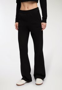 Czarne, wysokie dresy o luźnym kroju i elastycznym pasku w talii. Materiał jest miękki, bez widocznych wzorów. Zestawione z białymi trampkami.