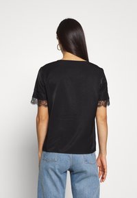 Sort kortærmet top med blonder ved ærmerne, glat tekstur, afslappet pasform og bred halsudskæring. Båret med lyseblå denimjeans.