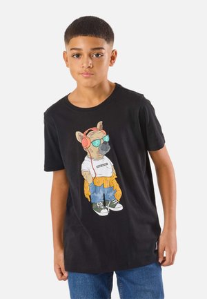 Ragazzo con maglietta nera con cane dei cartoni animati con occhiali da sole, cuffie, guanti e abbigliamento casual, abbinata a jeans blu, in piedi contro uno sfondo bianco.