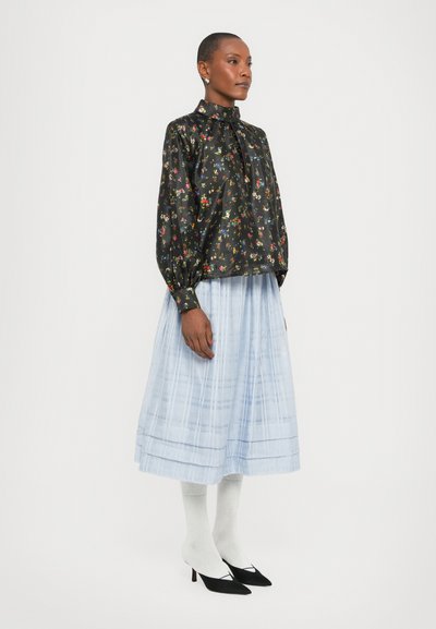 Blusa nera floreale con maniche a sbuffo, abbinata a una gonna plissè azzurro chiaro, calze bianche e décolleté neri a punta.