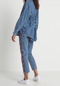 Jeansskjorta med volangdetalj på baksidan, ihopparat med ljusblå jeans med sidostripes i röd och vit, samt vita sneakers.