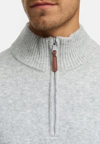 Grå zip-up tröja med ribbat krage, som har en halvdragkedja framtill med ett brunt läderdragband. Mjuk textur och ren design.