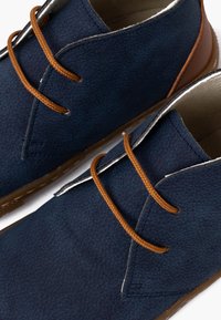Stivaletti alla caviglia in suede blu texturizzato con lacci e tab della tacco marroni, caratterizzati da una punta arrotondata e dettagli di cucitura minimalisti.