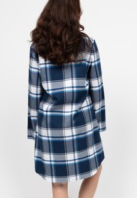 Abito camicia a quadri blu navy e grigio con maniche lunghe, orlo rotondo e texture morbida. Presenta linee di accento bianche e azzurre chiare nel motivo.