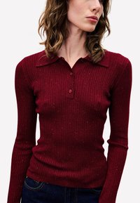 Bordeaux geribbelde gebreide polo met een kraag, met drie knopen op de knoopsluiting en een gestructureerde uitstraling met subtiele spikkels.