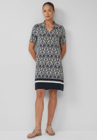 Kurzärmliges Kleid in Marineblau mit einem weißen Blättermuster, ausgestattet mit einem kragenlosen Ausschnitt und einem kontrastierenden weißen Saum.