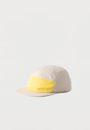 Casquette beige à cinq panneaux avec panneau avant jaune et trous de ventilation verticaux sur le côté sur fond blanc.