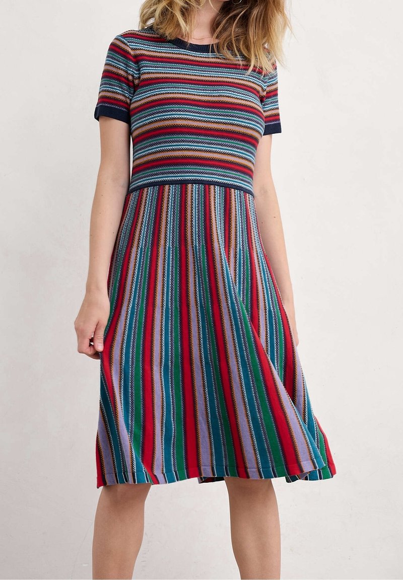 Femme portant une robe à manches courtes, longueur genou, avec des rayures horizontales sur le haut et des rayures verticales multicolores sur la jupe.