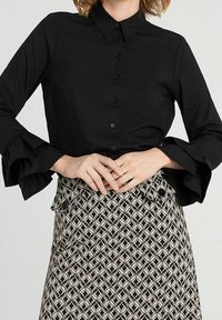 Svart skjorta med knappar och långa, volangärmar; matchad med en mönstrad kjol i krämfärgad och svart geometrisk design.