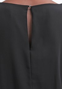 Vêtement noir avec une fente dans le dos et une fermeture à boutons au niveau du cou. Texture lisse avec un design simple, sans motifs ni accents supplémentaires.