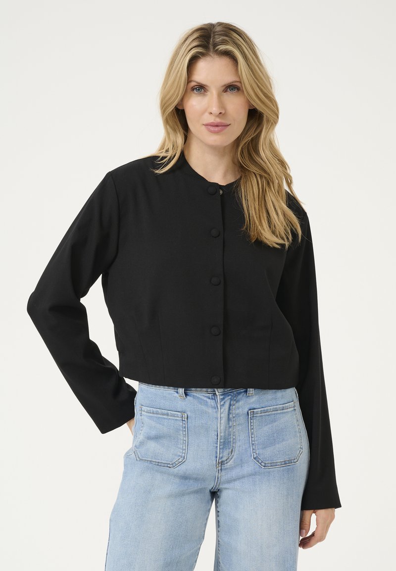 Schwarze cropped Jacke mit Rundhalsausschnitt, vorderem Knopfverschluss und langen Ärmeln, kombiniert mit hellblauen hoch taillierten Jeans.