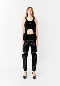 Top corto negro con recortes, que presenta un logo. Pantalones negros con bolsillos con cremallera, detalles en cuero y ribetes blancos. Tacones negros de punta.