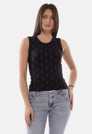 Donna che indossa un top nero senza maniche con strisce verticali bianche e jeans a vita alta color azzurro chiaro, in piedi con una mano in tasca.