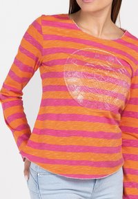 Langärmliges Oberteil in orange- und pinkfarbenen horizontalen Streifen, mit einem runden, glitzernden Grafikdesign. Hergestellt aus einem strukturierten Stoff mit abgerundetem Saum.