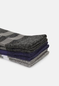 Stack of socks in four colors: dark gray, light gray, purple, and navy. Each sock features a ribbed texture and a patterned design.
